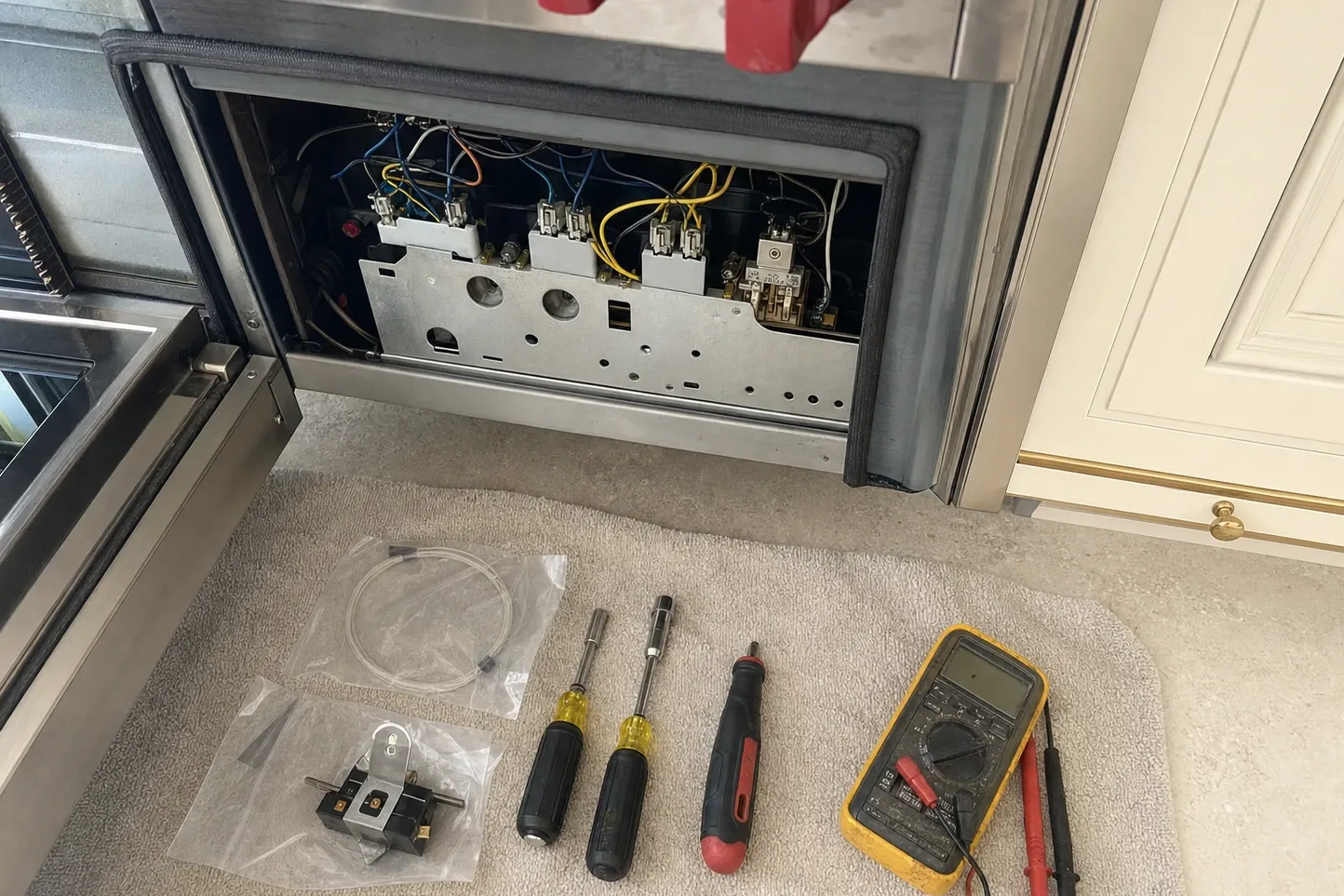 Open lower access panel exposing a bank of relays and wiring, with replacement parts still bagged on the floor beside nut drivers and a multimeter